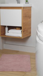 Photo of Pink mat near sink and tub on wooden floor in bathroom