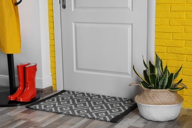 Hallway interior with beautiful houseplant, hanger stand and door mat on floor near entrance