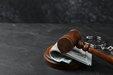 Judge's gavel, money and handcuffs on dark grey table. Space for text