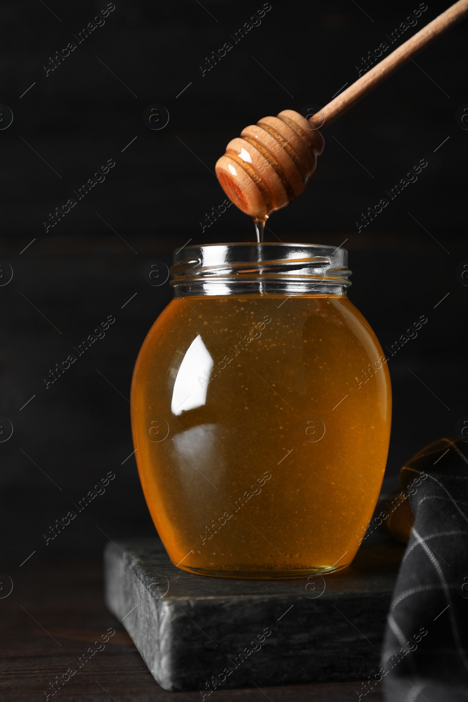 Photo of Jar of organic honey and dipper on wooden table against dark background