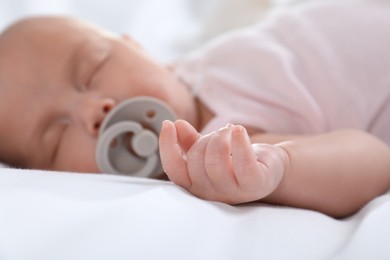 Photo of Cute little baby with pacifier sleeping at home, focus on hand