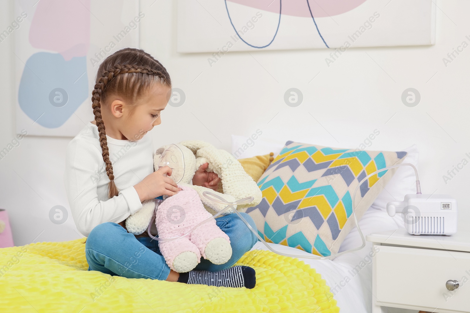 Photo of Little girl with toy bunny and nebulizer for inhalation on bed at home