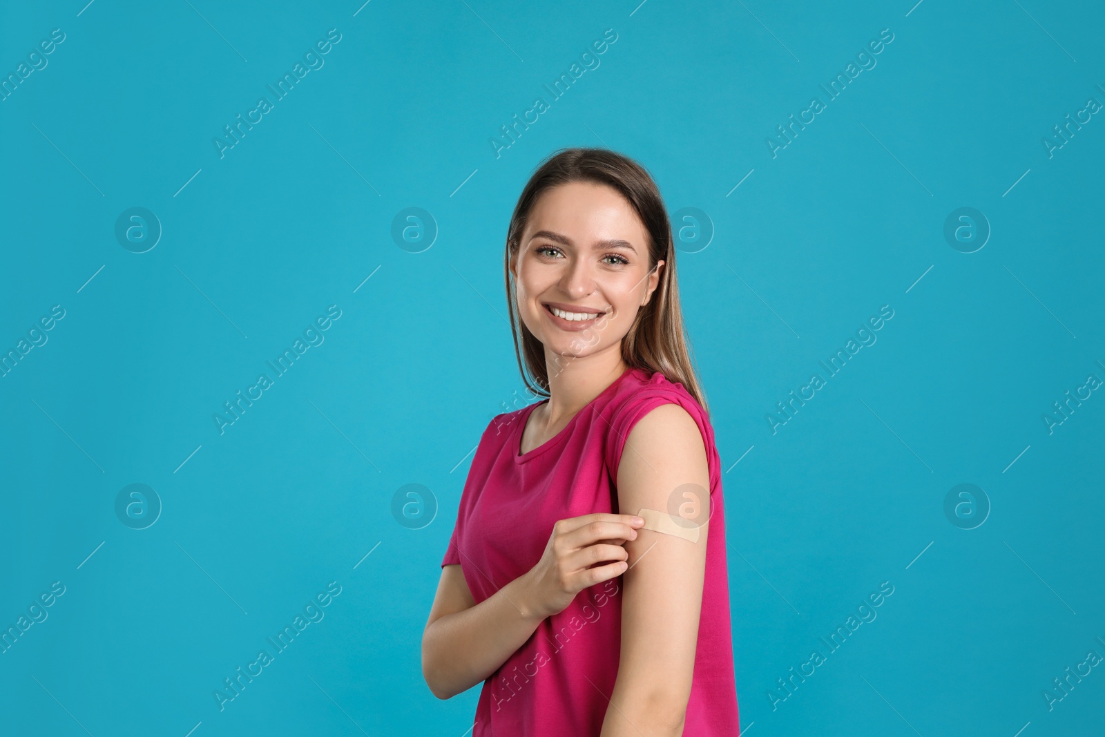 Photo of Vaccinated woman showing medical plaster on her arm against light blue background