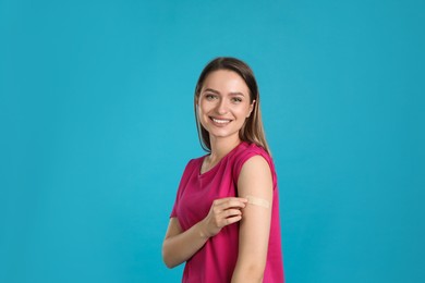 Photo of Vaccinated woman showing medical plaster on her arm against light blue background