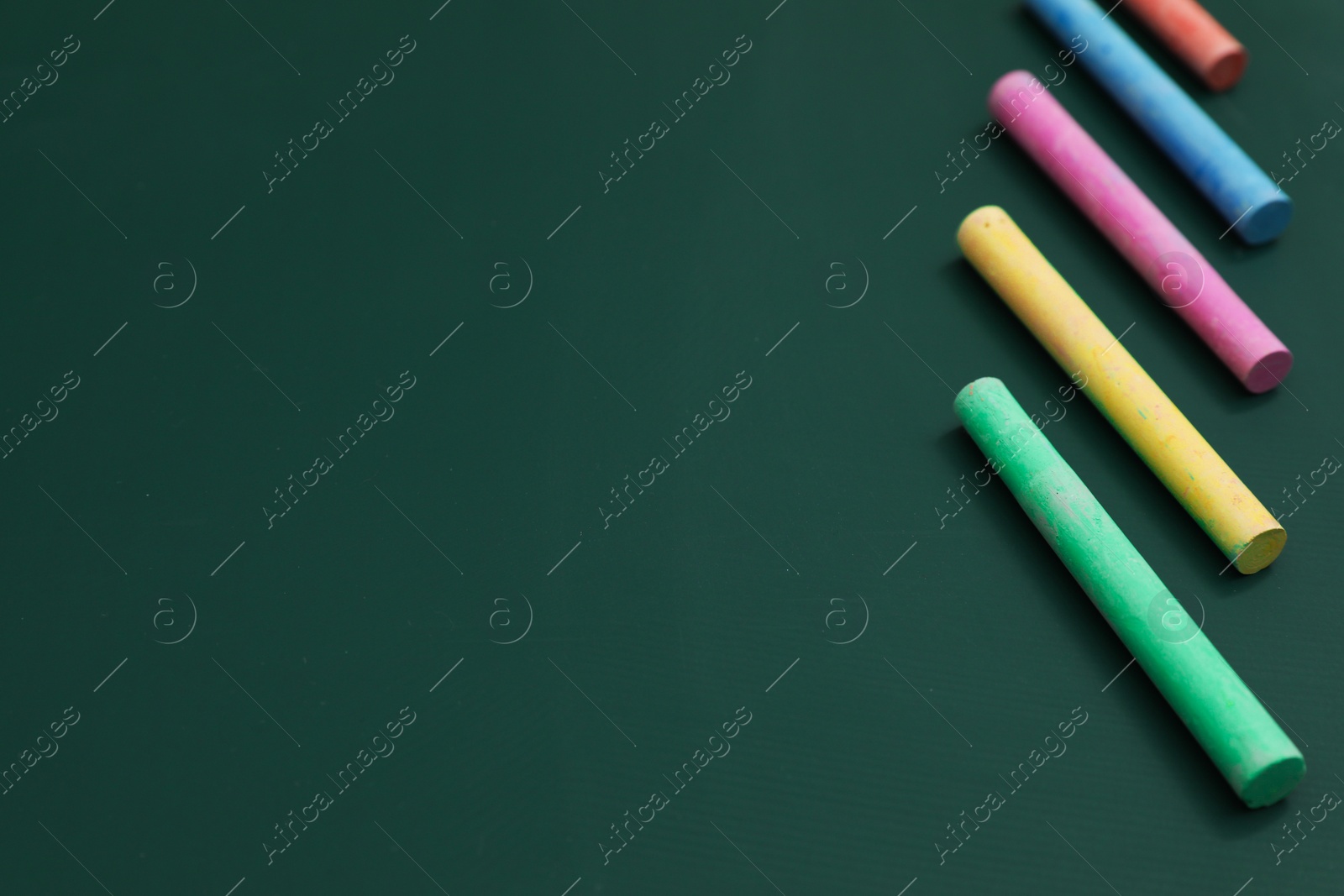 Photo of Colorful chalks on green board, closeup. Space for text