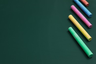 Photo of Colorful chalks on green board, closeup. Space for text