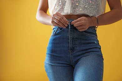 Woman unbuttoning jeans on yellow background, closeup