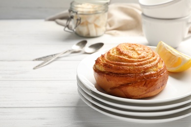 Stack of plates with tasty bun on white wooden table, space for text. Fresh from oven