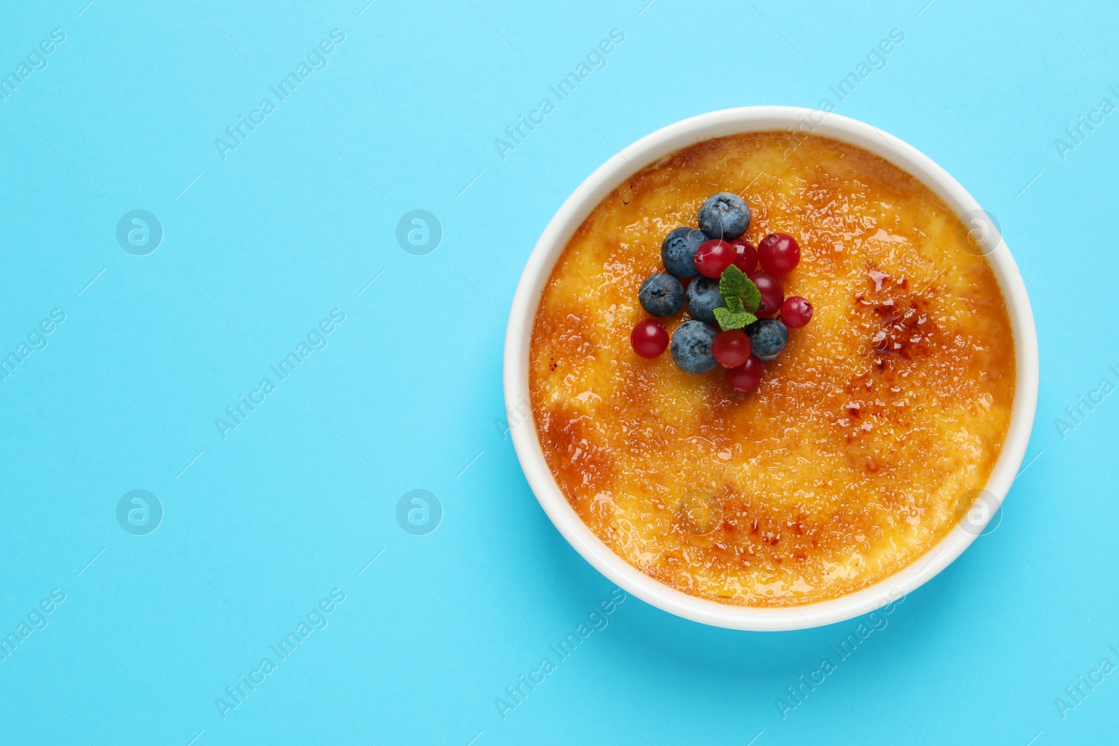 Photo of Delicious creme brulee with fresh berries and mint on light blue background, top view. Space for text