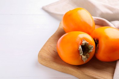 Photo of Board with delicious ripe persimmons on white wooden table, closeup. Space for text