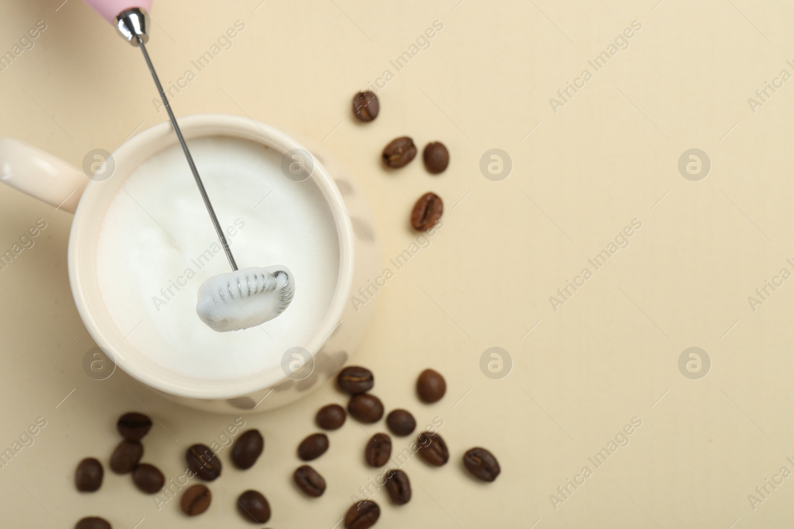 Photo of Mini mixer (milk frother), cup of whipped milk and coffee beans on beige background, flat lay. Space for text