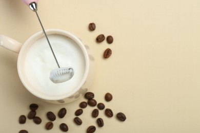 Mini mixer (milk frother), cup of whipped milk and coffee beans on beige background, flat lay. Space for text