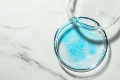 Photo of Petri dish with liquid and lid on white marble table, flat lay. Space for text