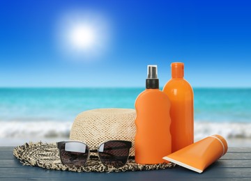 Image of Different skin sun protection products and beach accessories on blue wooden table against seascape. Space for design