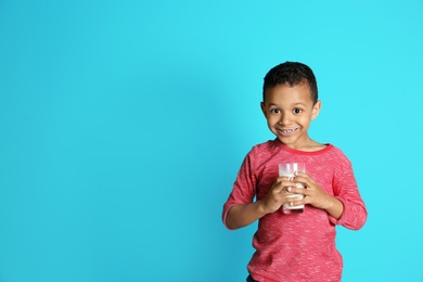 Adorable African-American boy with glass of milk on color background