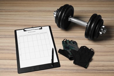 Photo of Clipboard with workout plan, dumbbell and cycling gloves on wooden table. Personal training