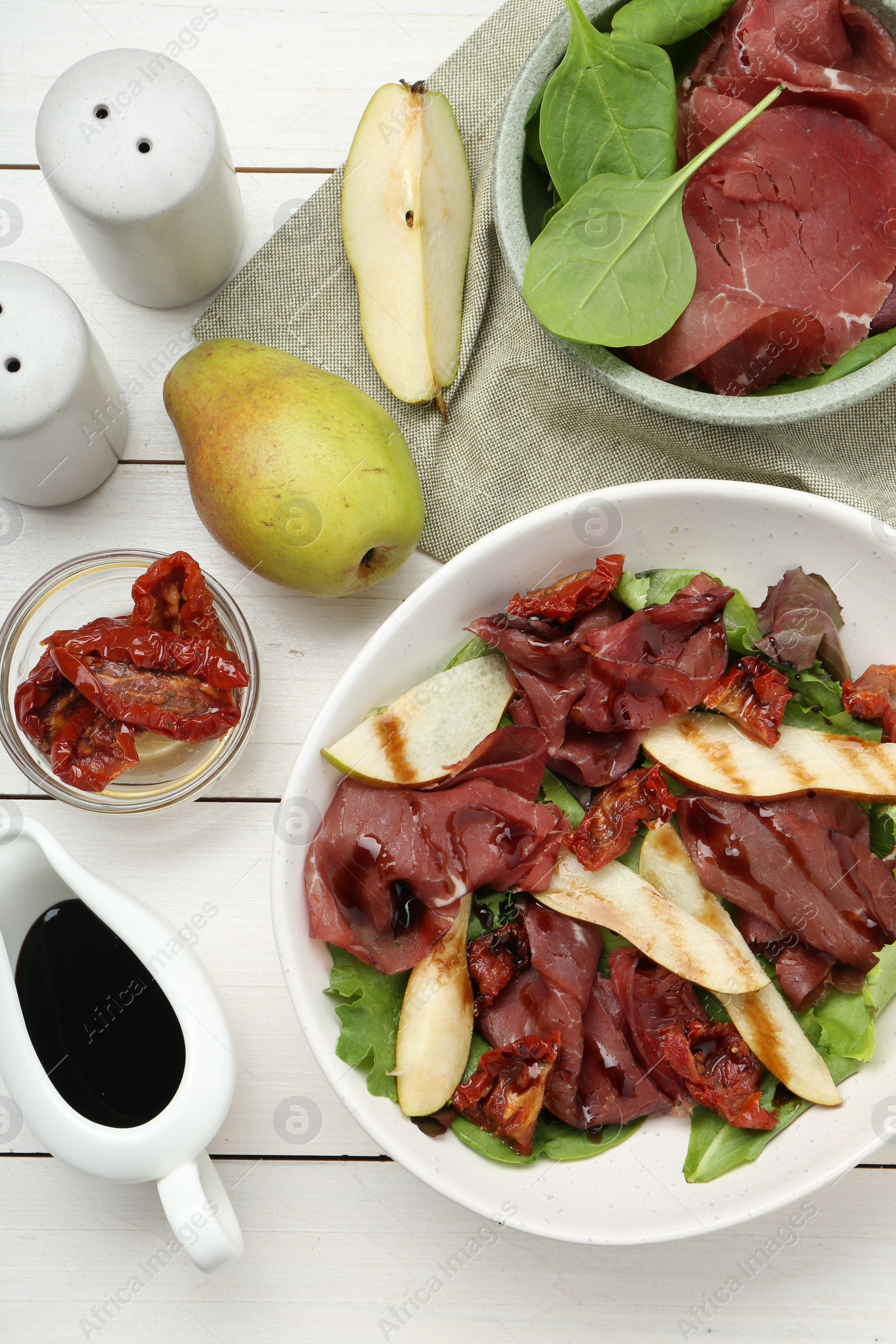Photo of Delicious bresaola salad with sun-dried tomatoes, pear and balsamic vinegar served on white wooden table, flat lay