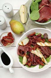 Delicious bresaola salad with sun-dried tomatoes, pear and balsamic vinegar served on white wooden table, flat lay