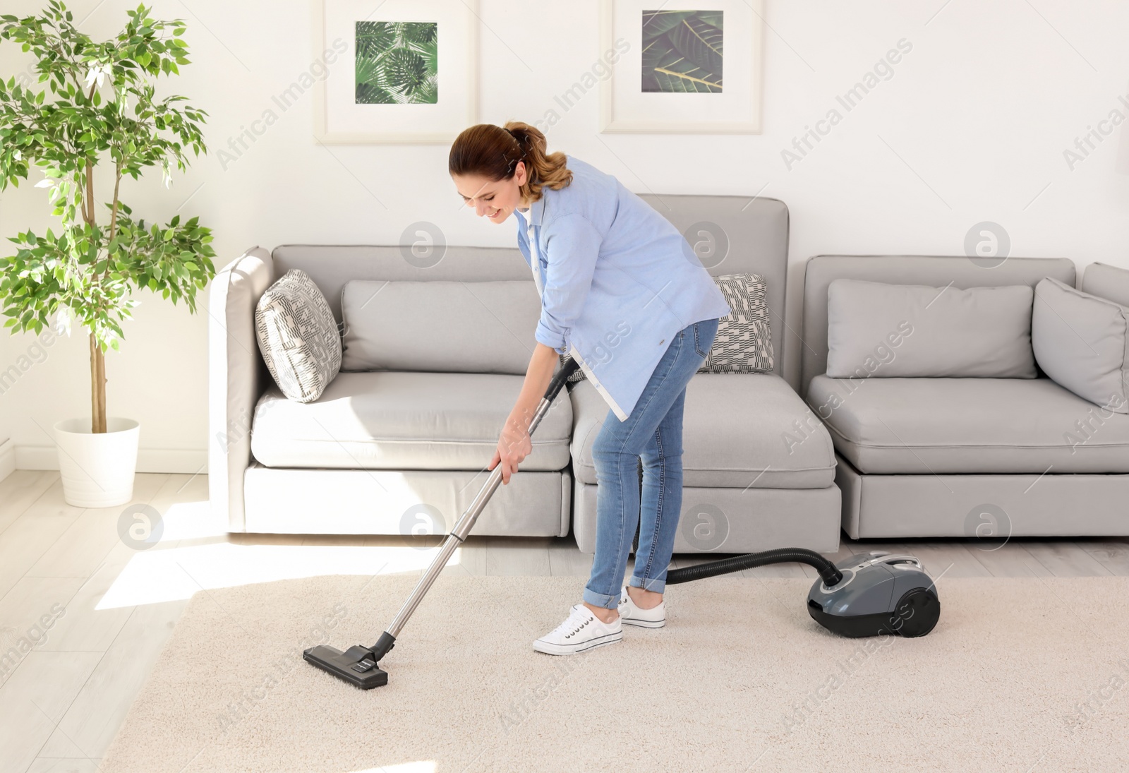 Photo of Woman removing dirt from carpet with vacuum cleaner at home