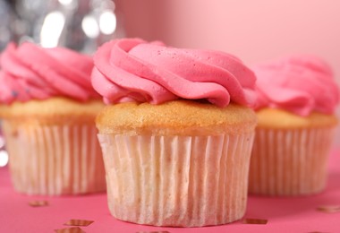 Photo of Delicious cupcakes with bright cream and confetti on pink table, closeup