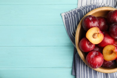 Photo of Delicious ripe plums in bowl on light blue wooden table, top view. Space for text