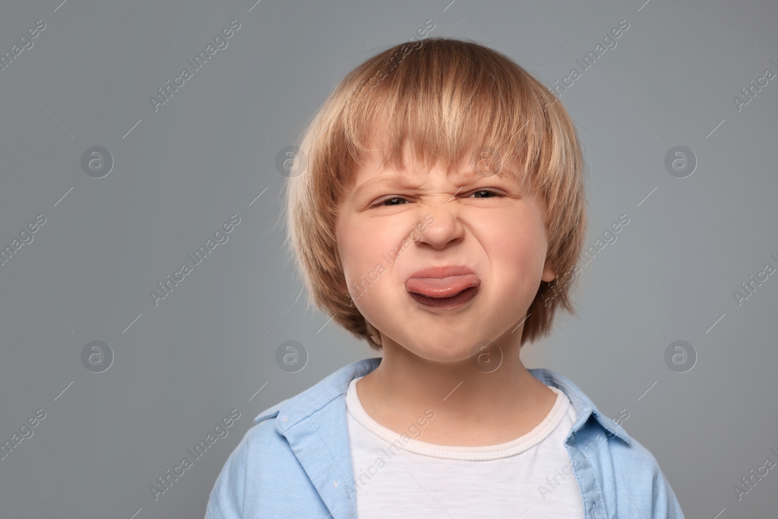 Photo of Cute little boy showing his tongue on grey background. Space for text