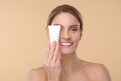 Photo of Woman holding tube of foundation on beige background