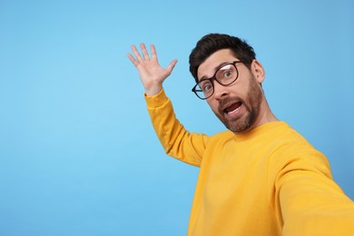 Photo of Emotional man taking selfie on light blue background, space for text