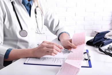 Doctor examining cardiogram at table in clinic, closeup