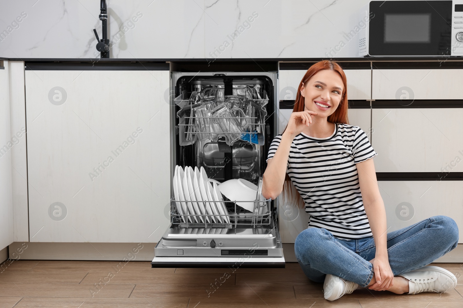 Photo of Smiling woman sitting near open dishwasher in kitchen