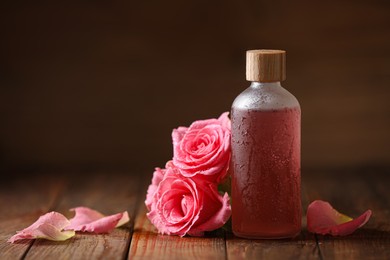 Bottle of essential rose oil and flowers on wooden table, space for text