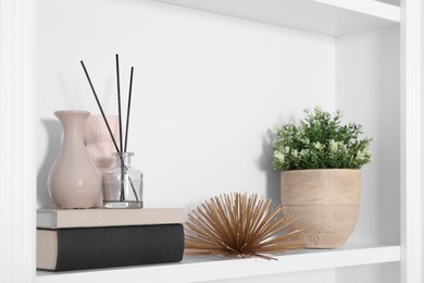 Interior design. Shelf with stylish accessories, potted plant and books near white wall