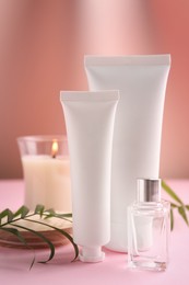 Photo of Different hand care cosmetic products, candle and green leaves on pink background
