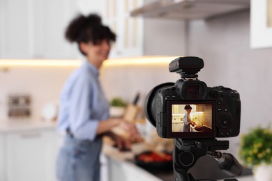 Photo of Food blogger cooking while recording video in kitchen, focus on camera