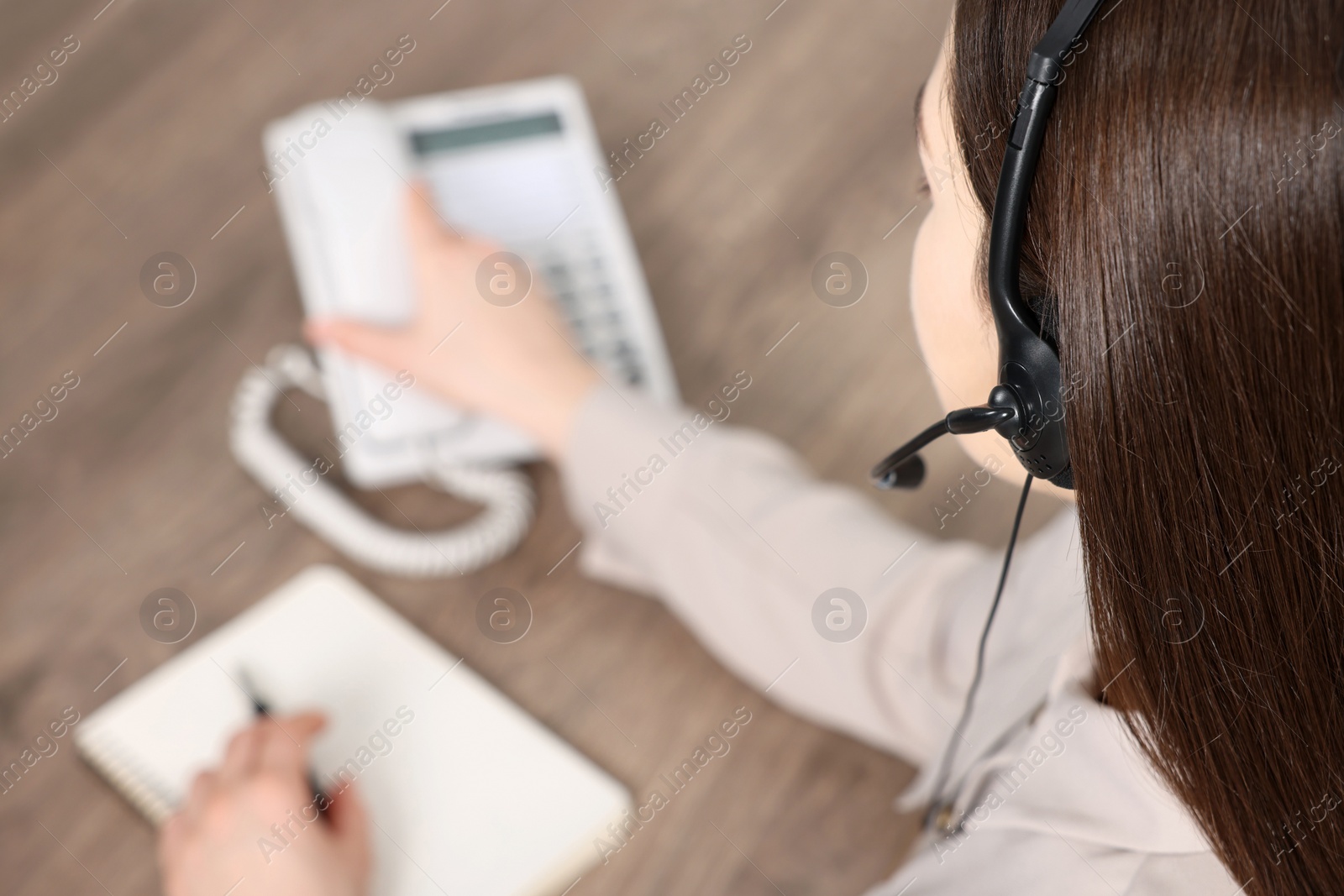 Photo of Hotline operator with headset and stationary phone working in office, closeup. Space for text