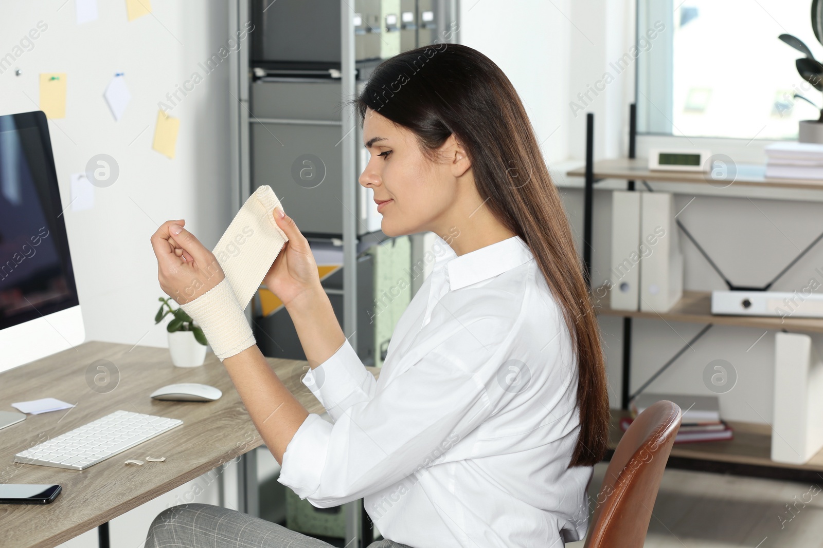 Photo of Young woman applying medical bandage onto wrist in office