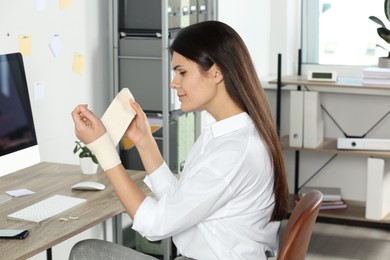 Young woman applying medical bandage onto wrist in office