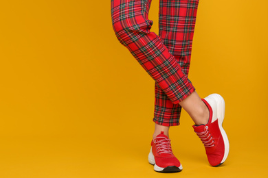 Photo of Woman wearing stylish sneakers on yellow background, closeup. Space for text