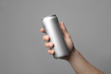 Photo of Man holding aluminum can with beverage on grey background, closeup. Space for design