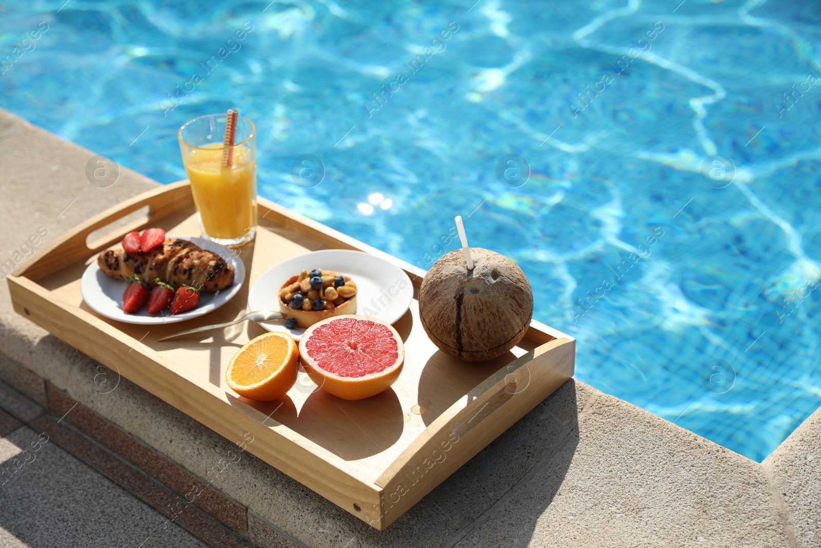 Photo of Tray with delicious breakfast near swimming pool