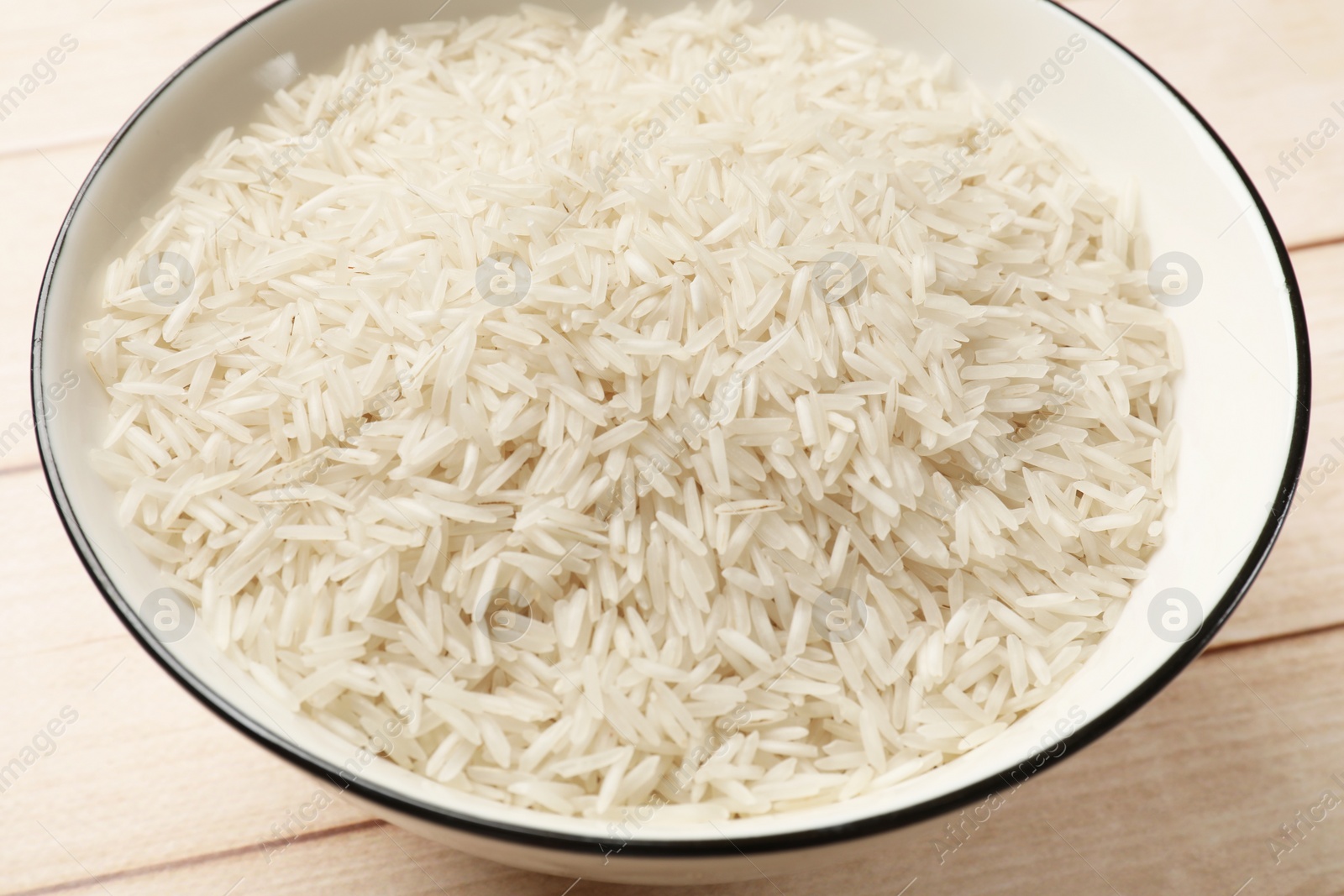 Photo of Raw basmati rice in bowl on white wooden table, closeup