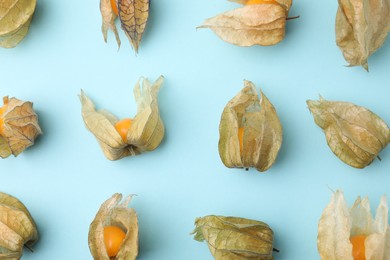 Photo of Ripe physalis fruits with calyxes on light blue background, flat lay