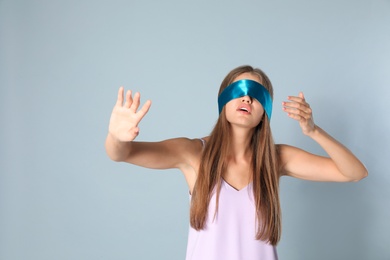 Young woman with light blue blindfold on grey background
