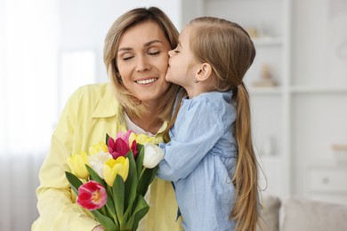 Photo of Little daughter kissing and congratulating her mom with Mother`s Day at home. Woman holding bouquet of beautiful tulips