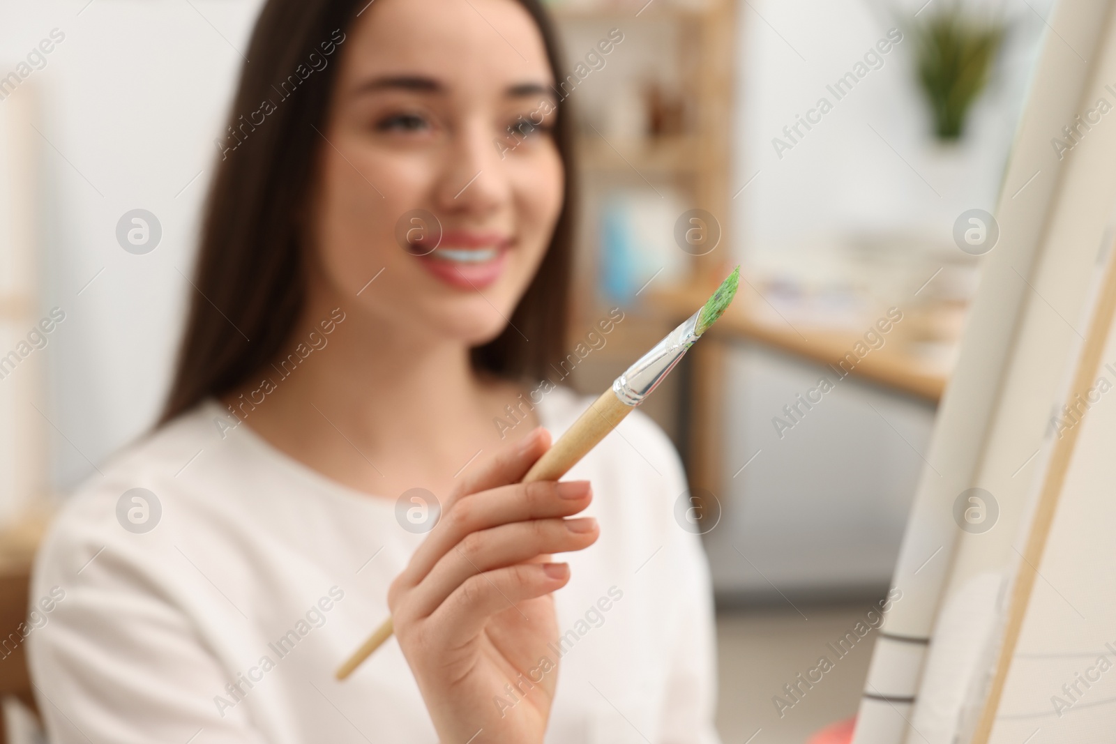 Photo of Beautiful young woman painting in studio, selective focus. Creative hobby