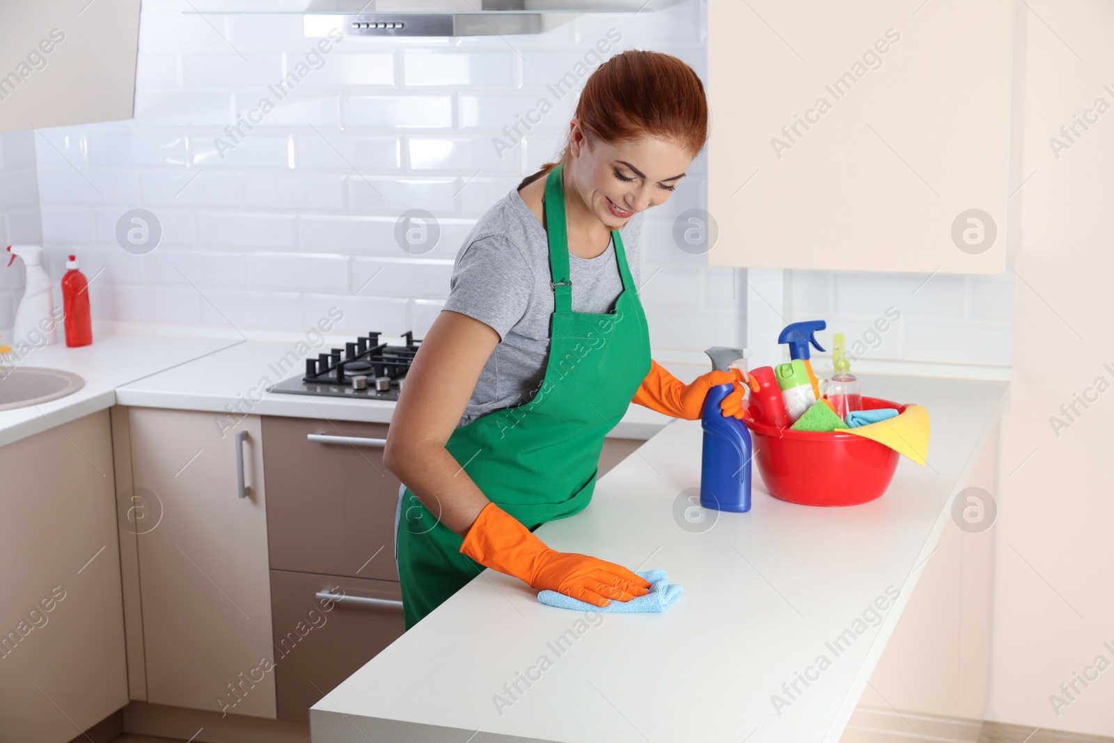 Photo of Woman in protective gloves cleaning kitchen table with rag, indoors