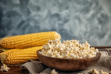 Photo of Bowl with delicious popcorn and cobs on table