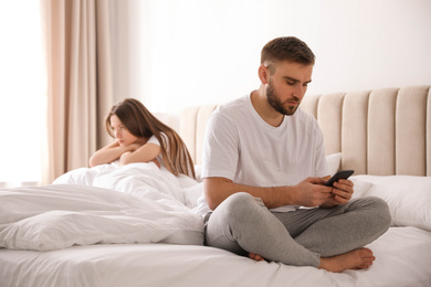 Young man preferring smartphone over his girlfriend on bed at home. Relationship problems