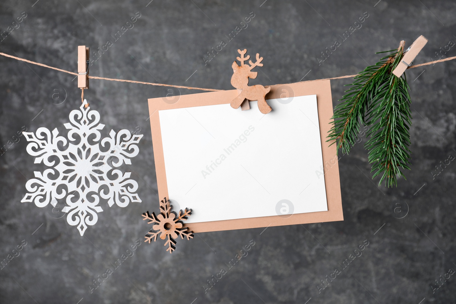 Photo of Blank Christmas card and festive decor on rope against grey background, space for text