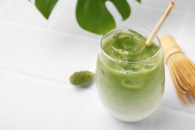 Glass of tasty iced matcha latte on white tiled table, closeup. Space for text